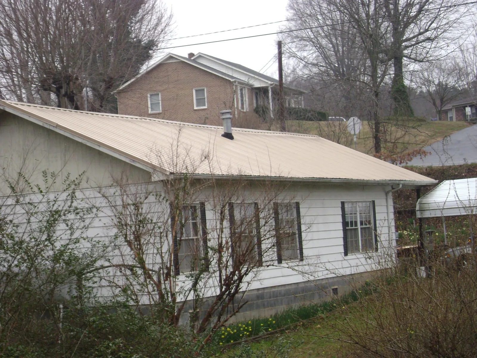 Tan metal roof on a white sided house set into a hillside — Commercial Roofing by Roofing Brothers in Ponte Vedra Beach